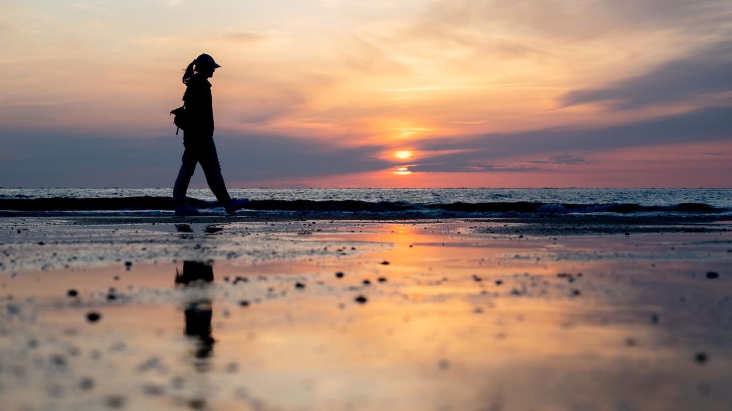 Eine junge Frau spaziert bei Sonnenuntergang am Strand entlang