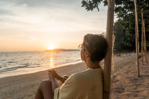 Wechseljahre: Frau sitz an Strand und schaut aufs Meer