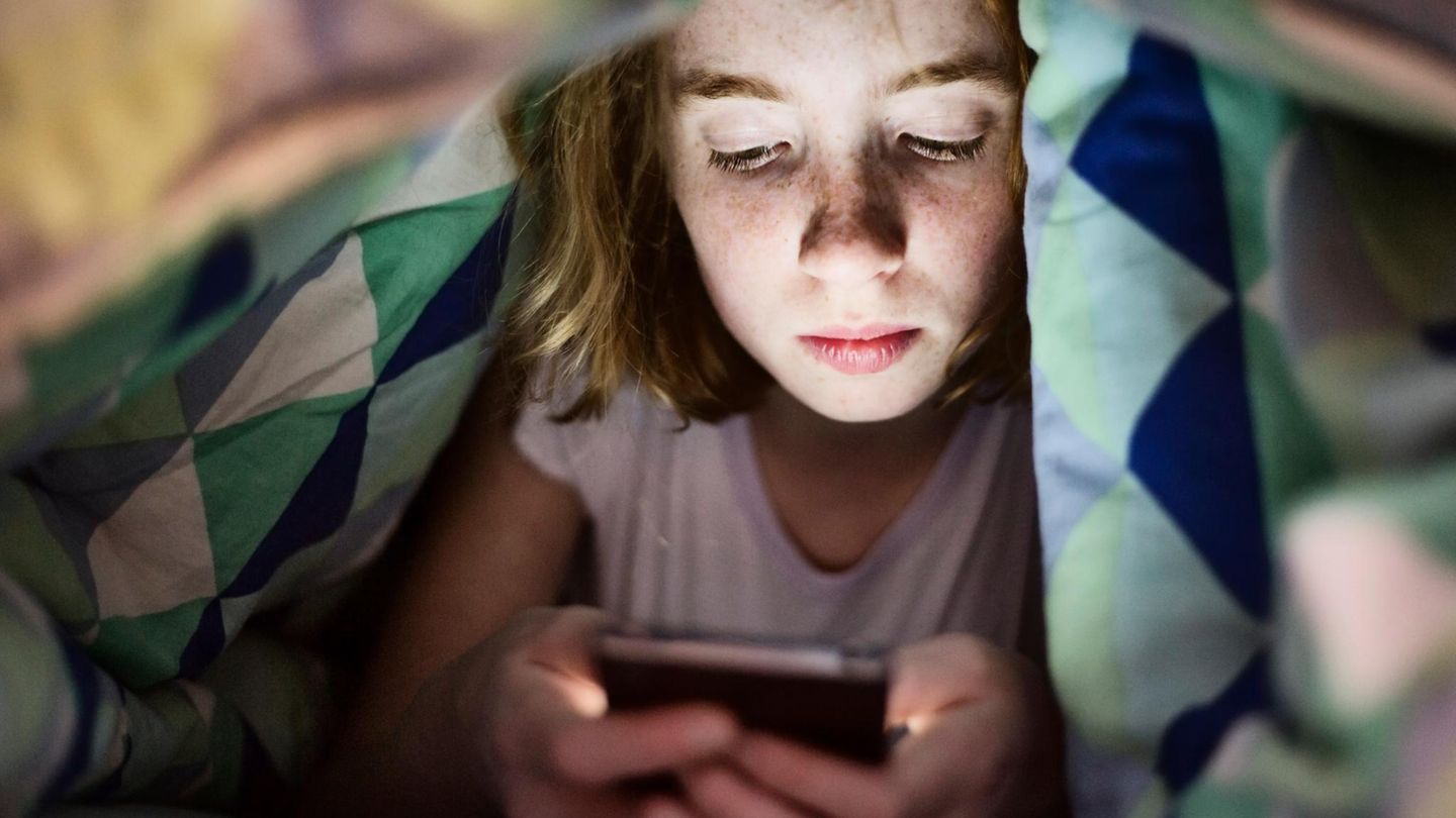 Ein Kind liegt mit dem Smartphone unter seiner Bettdecke