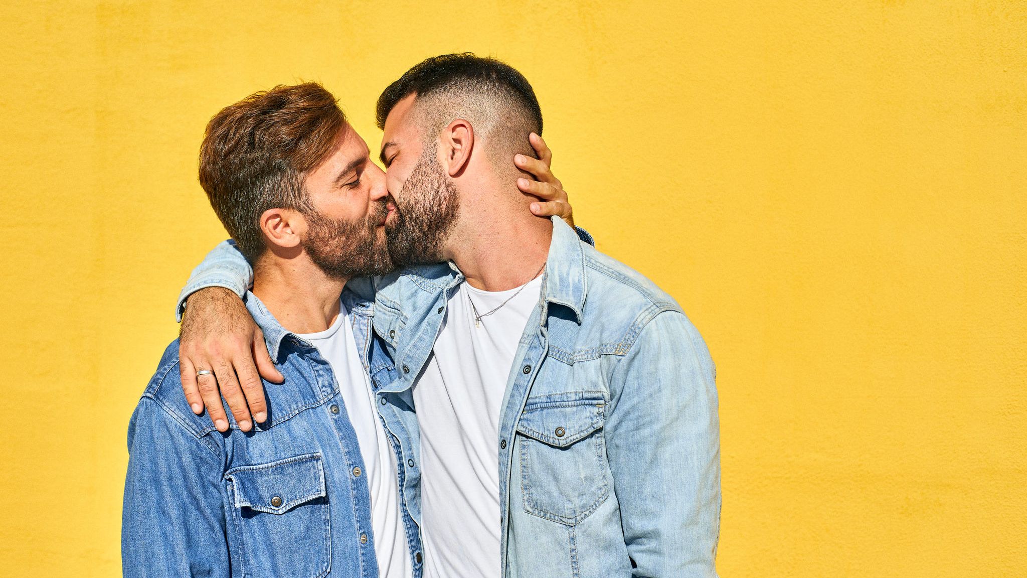 Homosexualität: Schwules Pärchen küsst sich vor einer gelben Wand