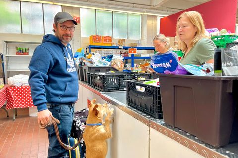 Tiertafel Mann mit Base Cap und blauem Hoodie und beigefarbener Hund stehen an Tresen zur Futterausgabe