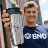 In einem Werbefoto hält jemand einen silbernen Kaffeebecher mit BND-Logo in die Kamera
