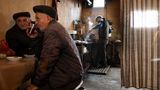 Männer sitzend am Tisch und im Hintergrund am Herd