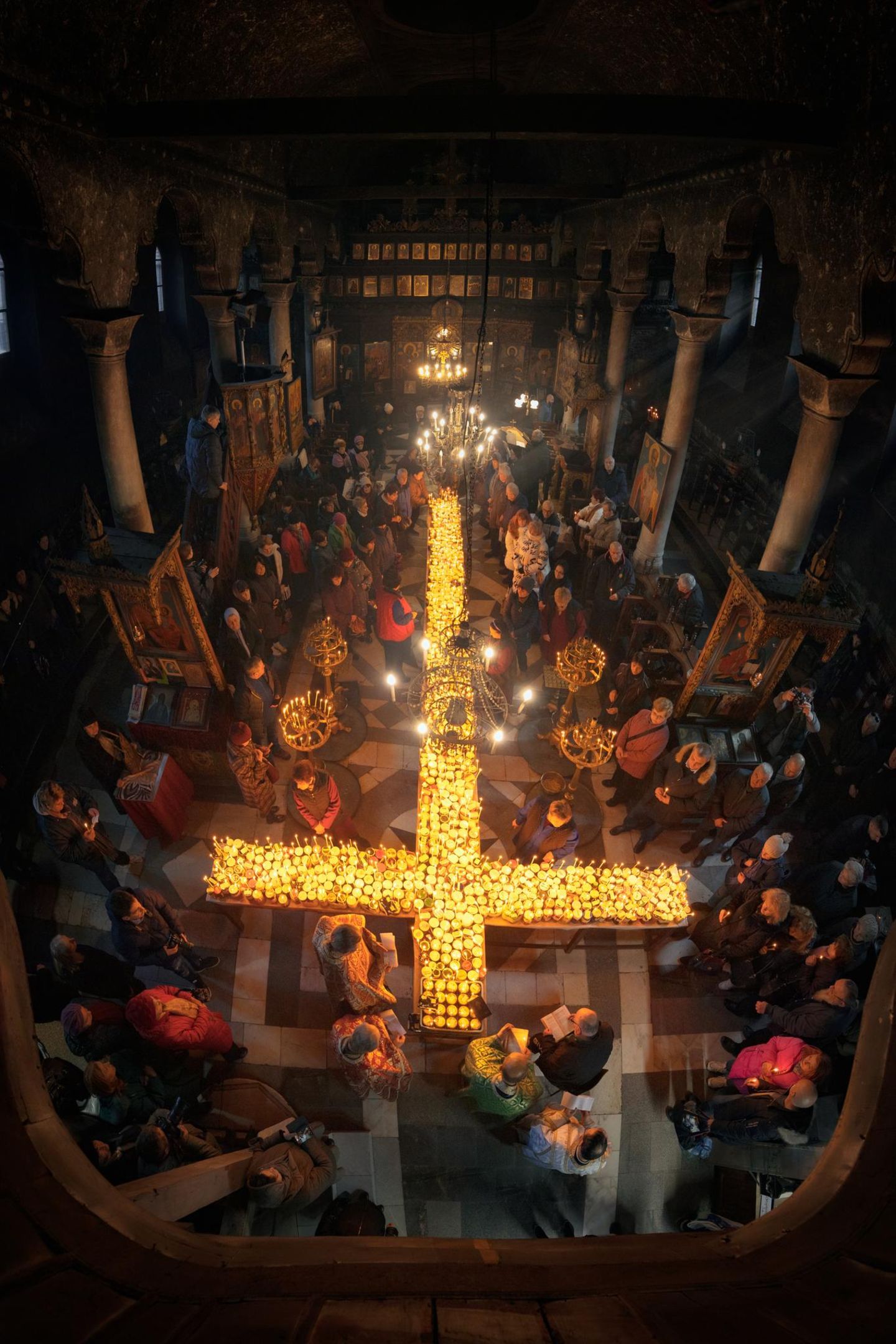 Im Kerzenschein Brennendes Kreuz in mitten vor betenden Menschen in einer Kirche