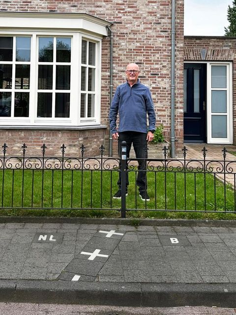 ein Mann steht in seinem Vorgarten in Baarle – mit einem Fuß in Belgien, mit dem anderen in den Niederlanden