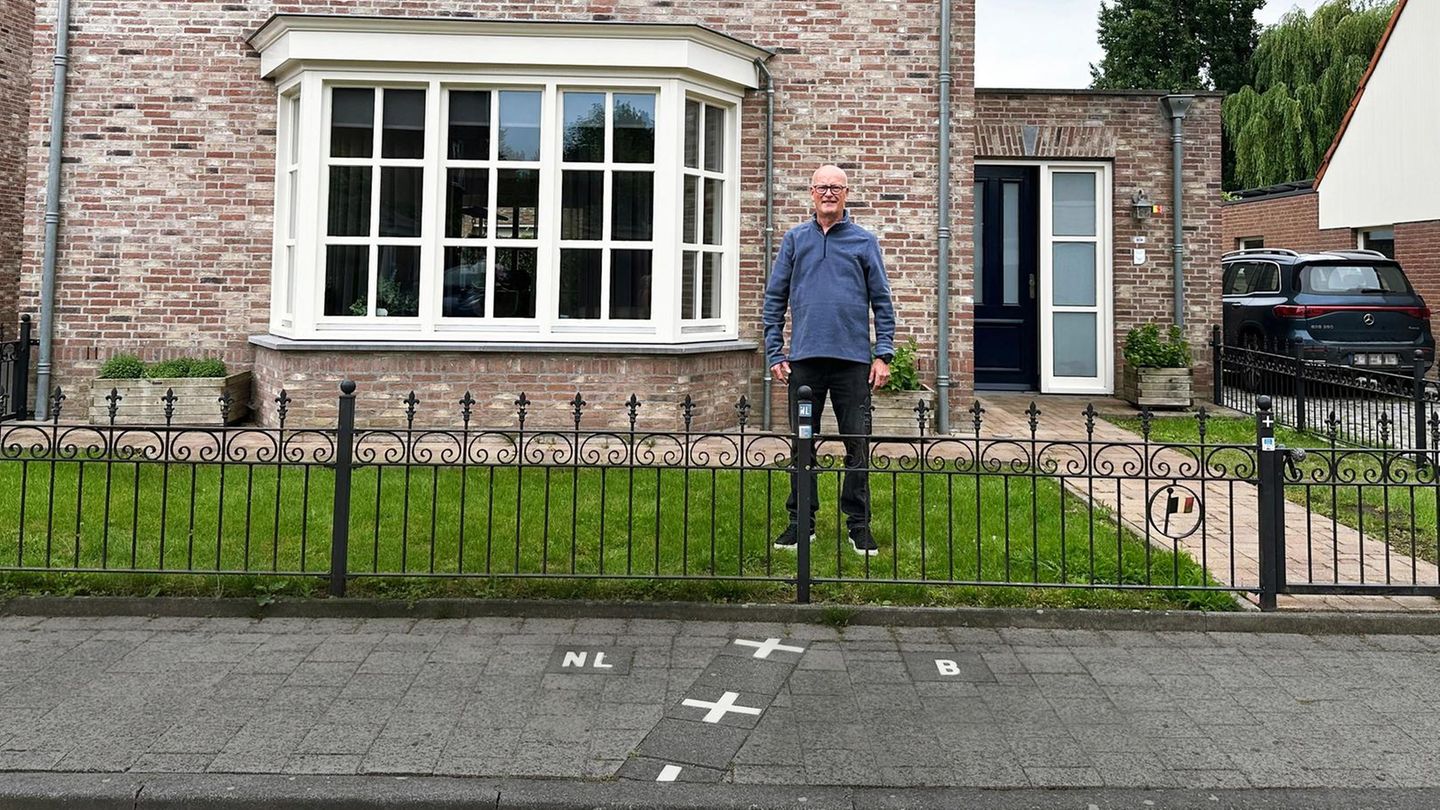 ein Mann steht in seinem Vorgarten in Baarle – mit einem Fuß in Belgien, mit dem anderen in den Niederlanden
