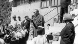 Der Dalai Lama steht vor Kindern und Erwachsenen und spricht
