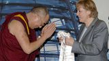 Angela Merkel hält einen weißen Seidenschal in den Händen, der Dalai Lama verbeugt sich.