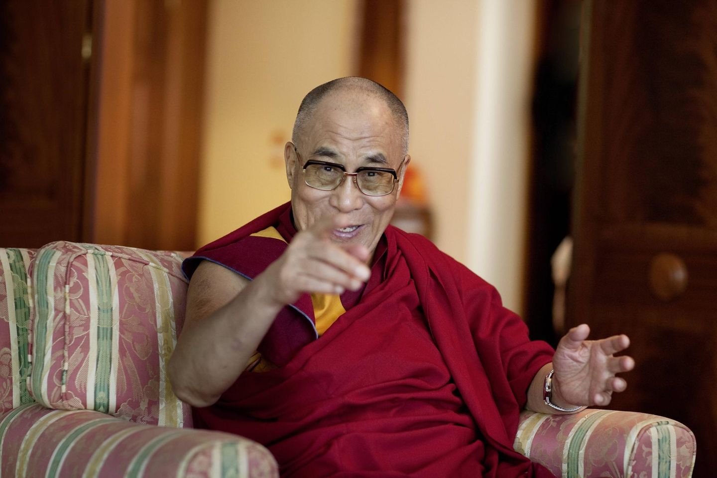 Der Dalai Lama lächelt und zeigt in die Kamera