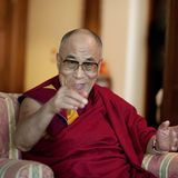 Der Dalai Lama lächelt und zeigt in die Kamera