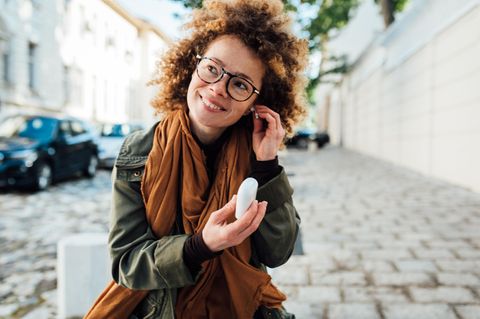 Eine Frau setzt sich Bluetooth-Kopfhörer ins Ohr