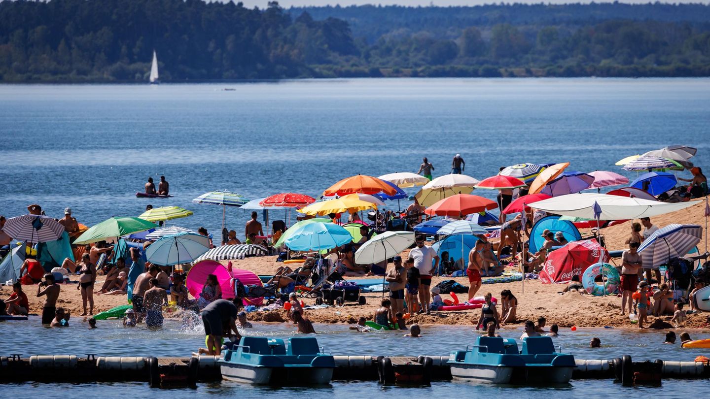 Unter Sonnenschirmen liegen Badegäste am Brombachsee in Bayern