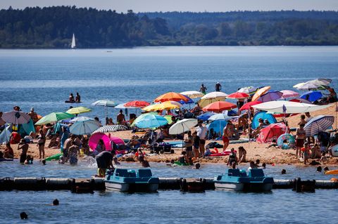 Unter Sonnenschirmen liegen Badegäste am Brombachsee in Bayern