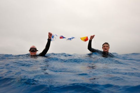 Zwei Männer im Wasser und halten Fahnen in der Hand hoch