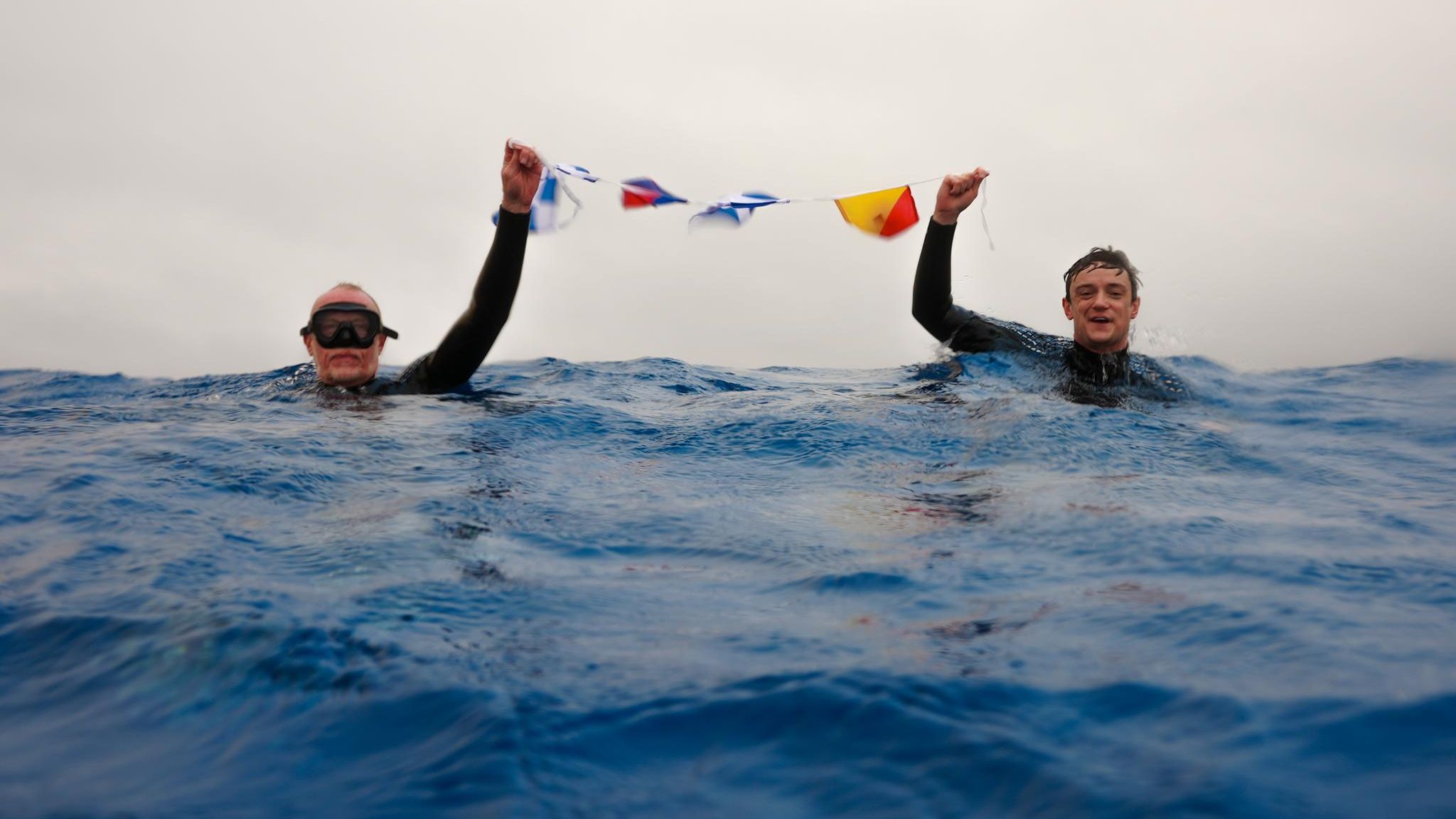 Zwei Männer im Wasser und halten Fahnen in der Hand hoch