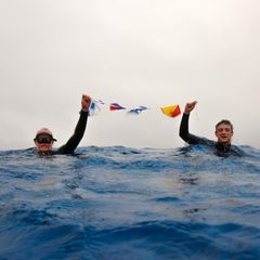 Zwei Männer im Wasser und halten Fahnen in der Hand hoch