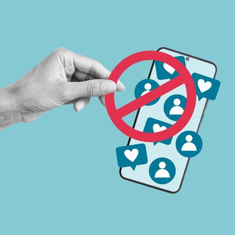 Social media ban: A hand holds a red ban on a cell phone with social media symbols