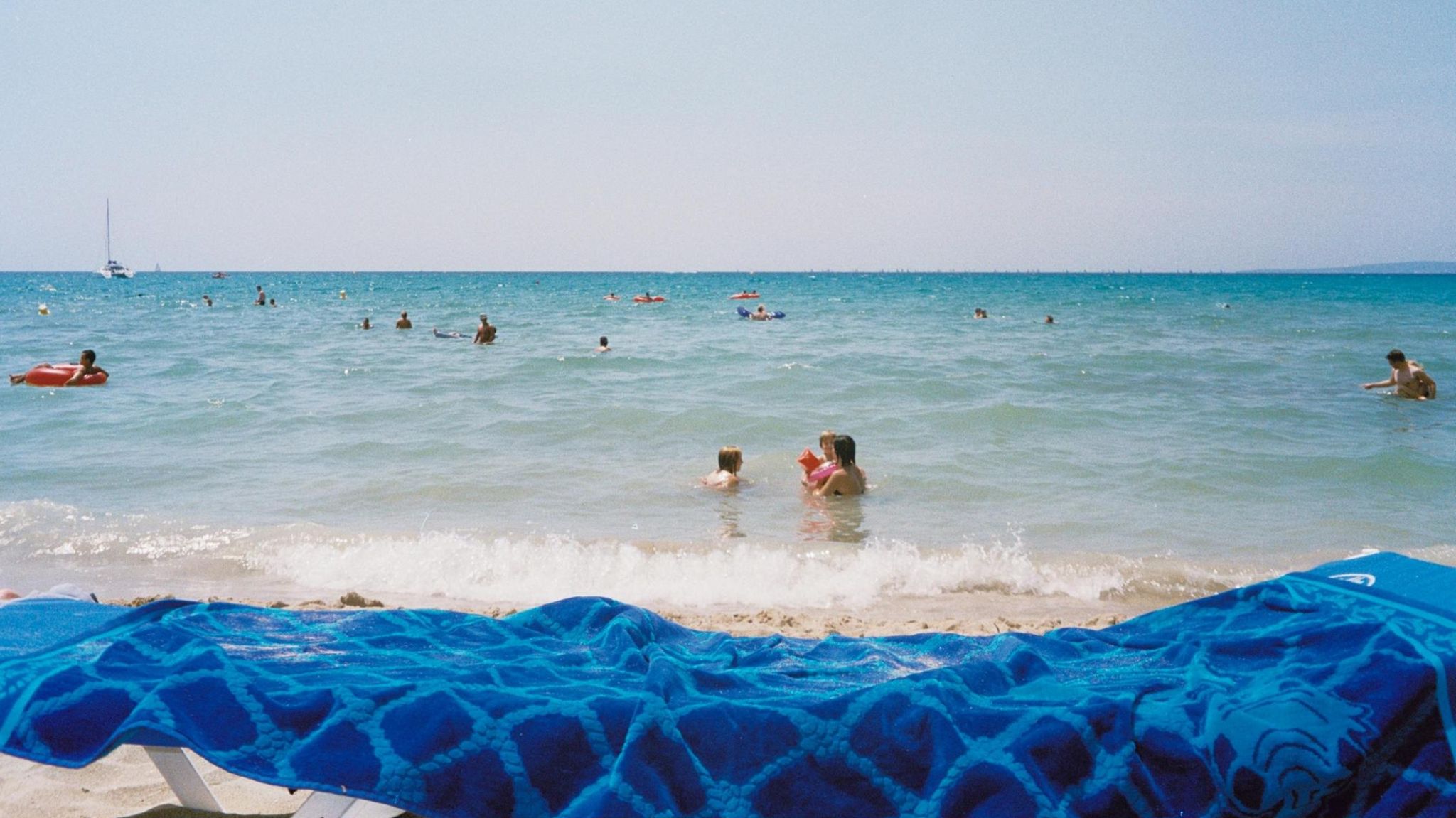 Menschen im Meer, im Vordergrund Sand und ein Badelaken
