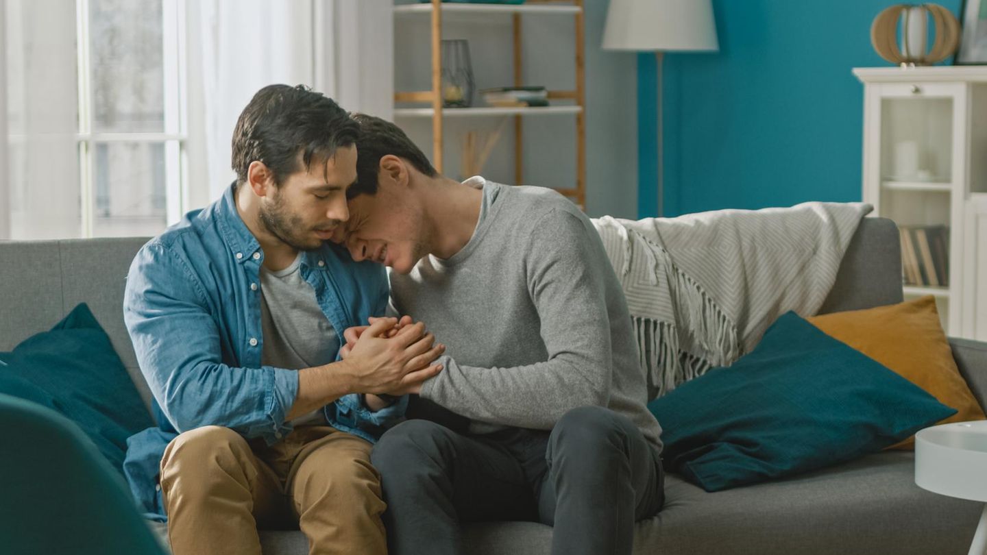 Ein Paar in einer Beziehung sitzt auf der Couch, einer der beiden Männer weint