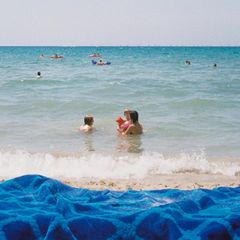 Menschen im Meer, im Vordergrund Sand und ein Badelaken