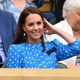 Kate in einem blauen Kleid mit weißen Punkten in der Logo, sie streicht ihr Haar zurück