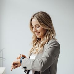 Glückliche Geschäftsfrau überprüft Smartwatch im Büro.