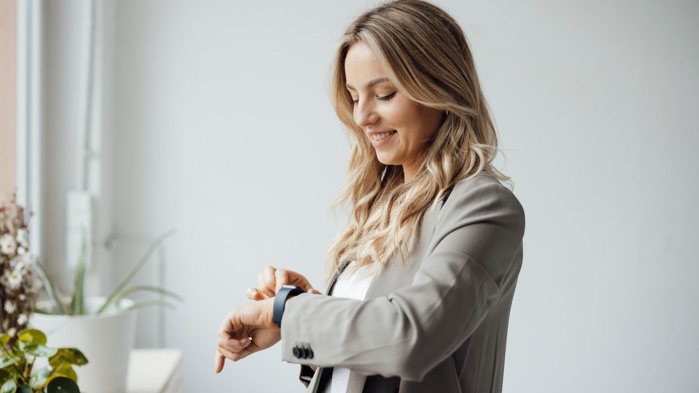 Glückliche Geschäftsfrau überprüft Smartwatch im Büro.