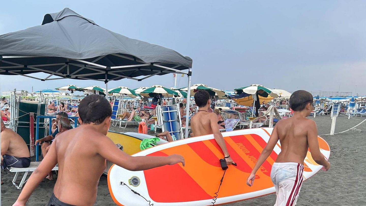 An einem Strand in Italien gehen drei Jungen mit einem SUP zum Wasser