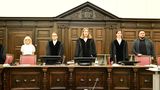 Zwei Frauen und ein Mann in schwarzen Roben stehen hinter der Richterbank im Block-Prozess, eingerahmt von
