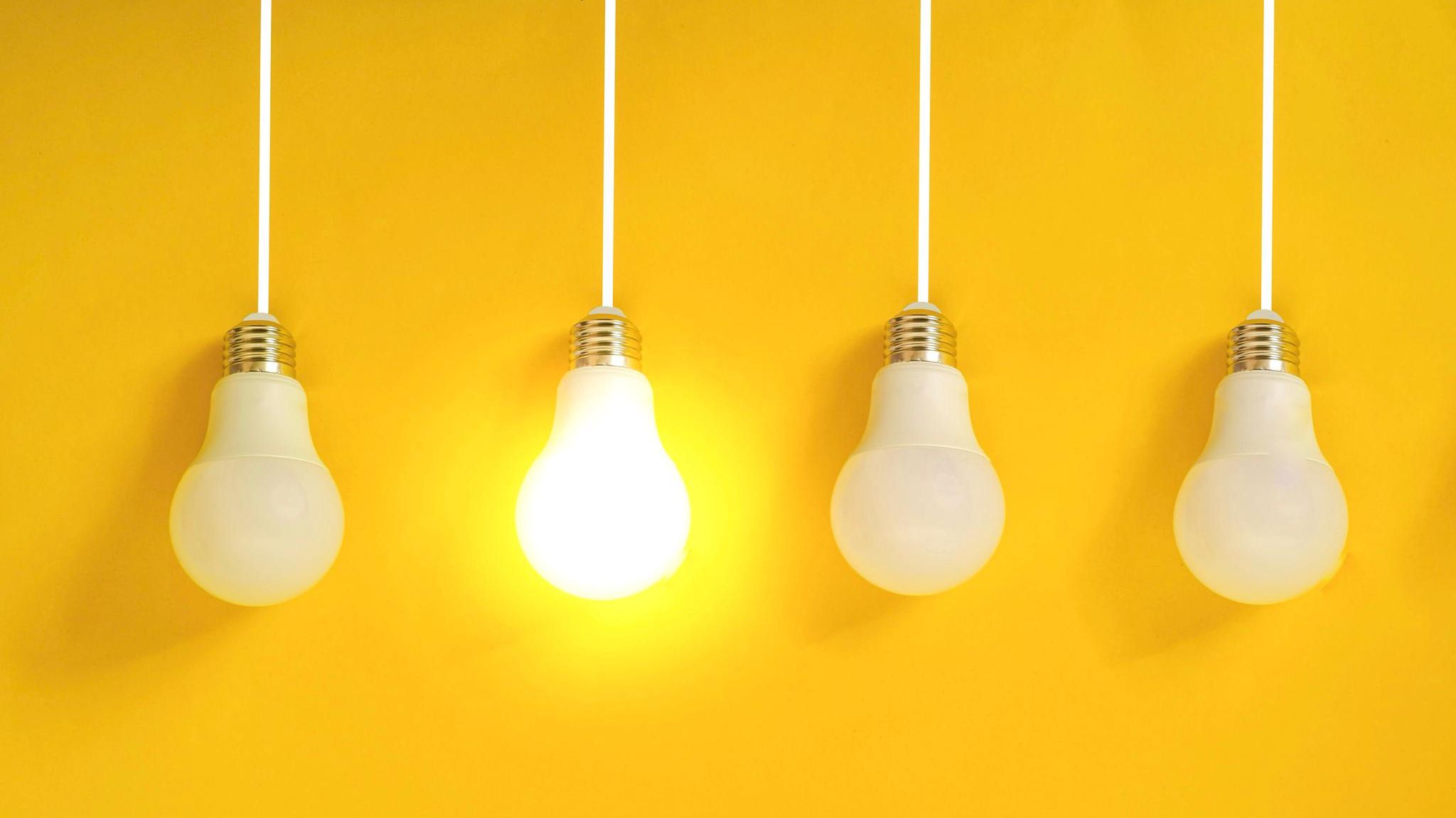 Hochbegabung: Vier Glühlampen vor gelber Wand. Eine Lampe leuchtet