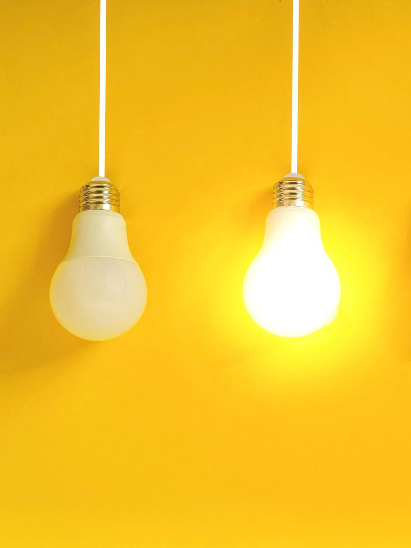 Hochbegabung: Vier Glühlampen vor gelber Wand. Eine Lampe leuchtet