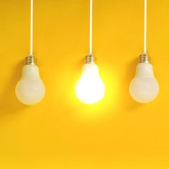 Hochbegabung: Vier Glühlampen vor gelber Wand. Eine Lampe leuchtet