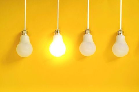 Hochbegabung: Vier Glühlampen vor gelber Wand. Eine Lampe leuchtet