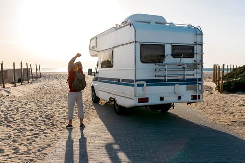 Urlaub: Mann neben Wohnmobil am Strand
