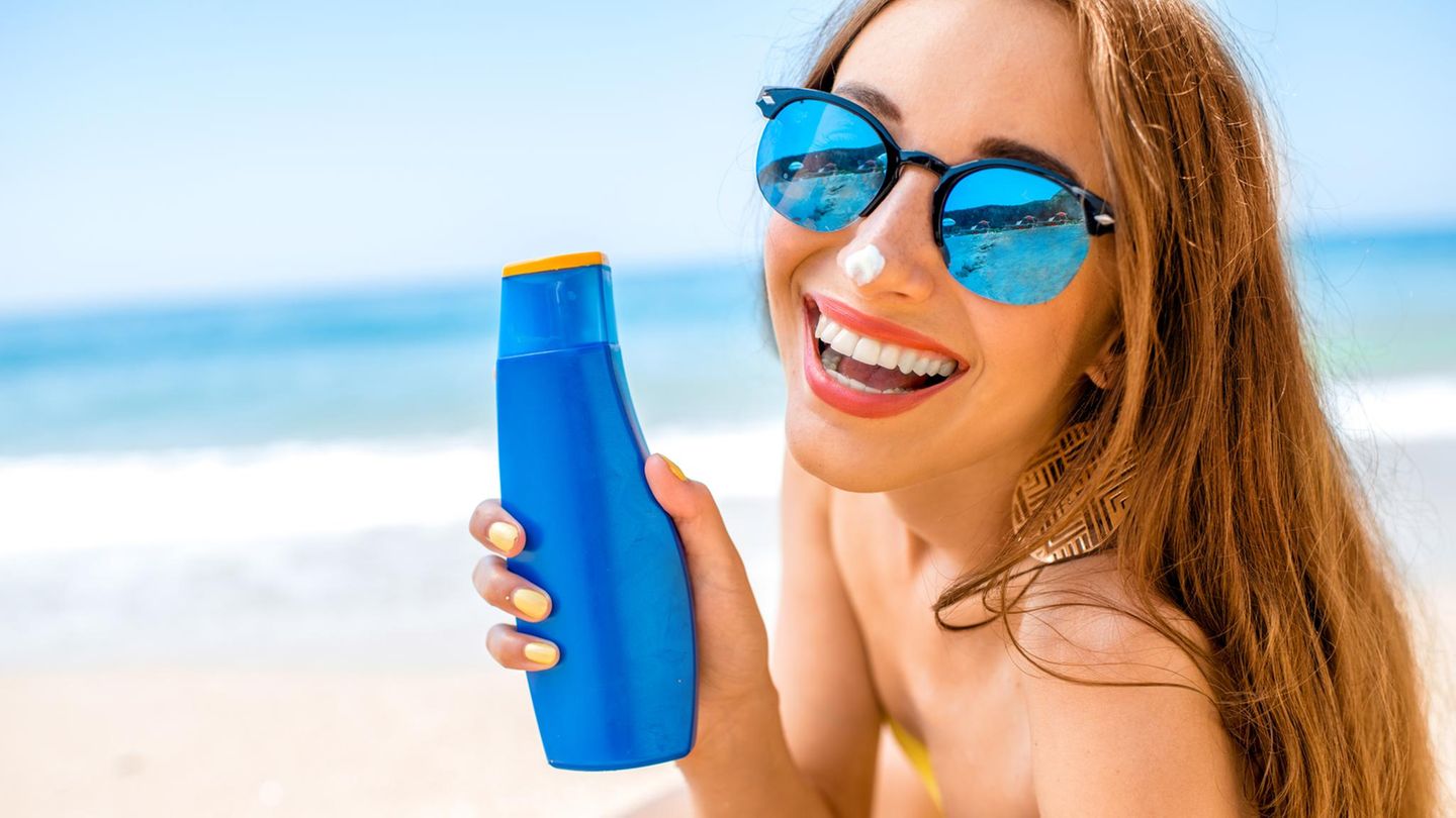 Frau zeigt Sonnencremeflasche am Strand.