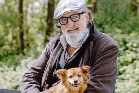 Andreas Hoppe mit Schiebermütze, schwarzer Brille und grauem Bart. Er hält seinen Hund im Arm