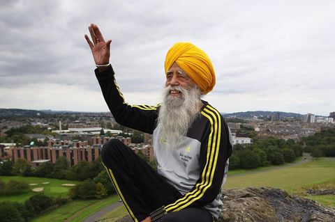 Fauja Singh, ein Mann in Trainingsanzug mit langem, grauen Bart und Turban, winkt