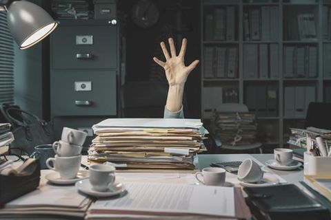 Eine Hand kommt hinter einem Aktenstapel hervor