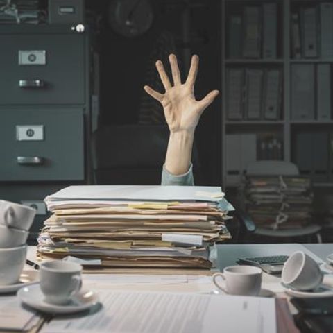 Eine Hand kommt hinter einem Aktenstapel hervor