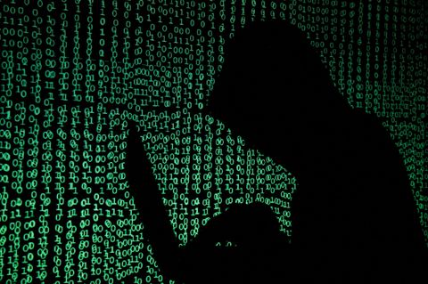 Ein Mann mit Kapuze hält einen Laptop in der Hand, während auf dem Bild ein Cybercode projiziert wird