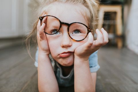 In Kind schaut geleingweilt mit verrutschter Brille an der Nase