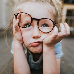 In Kind schaut geleingweilt mit verrutschter Brille an der Nase