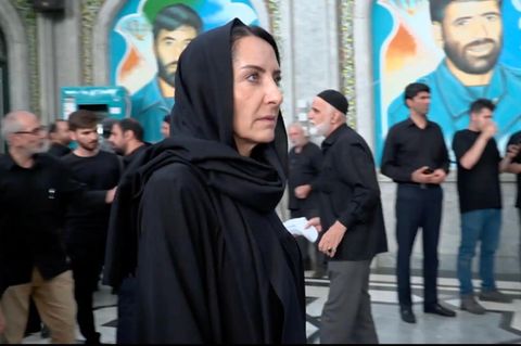 Reporterin steht verhüllt in schwarzer Kleidung in Teheran zwischen Menschen