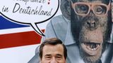 Wolfgang Grupp vor einem Plakat mit dem Trigema Maskottchen, dem Affen