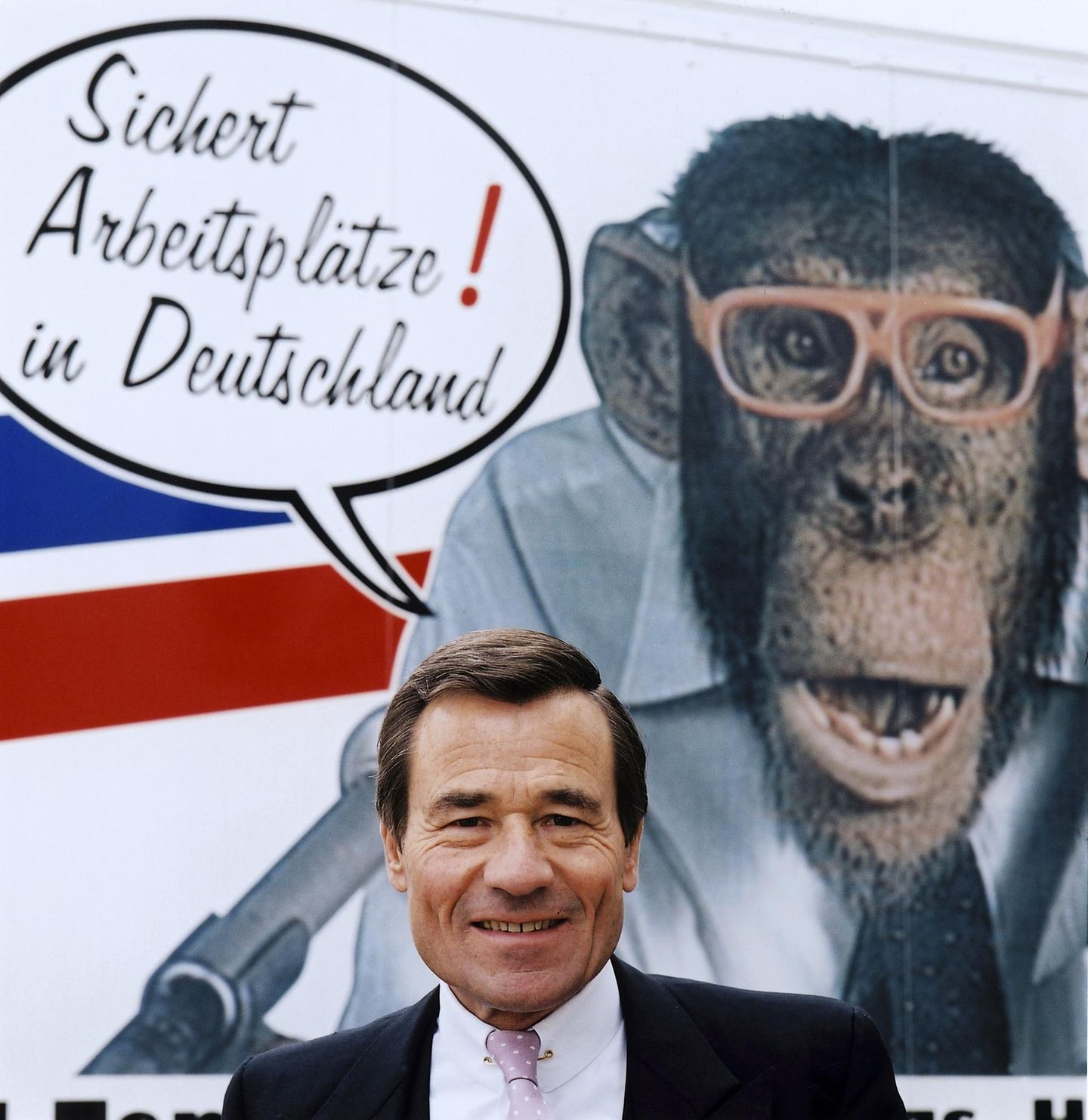 Wolfgang Grupp vor einem Plakat mit dem Trigema Maskottchen, dem Affen