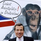 Wolfgang Grupp vor einem Plakat mit dem Trigema Maskottchen, dem Affen