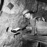 Ein Bergwerksleiter nimmt durch ein Loch in einer Steinwand eine Flasche entgegen