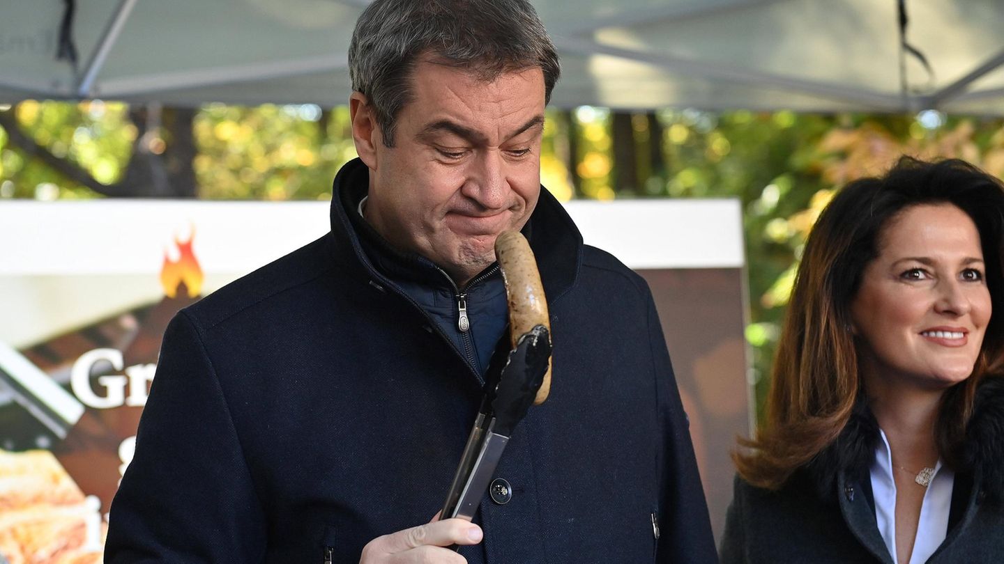 Markus Söder hält eine Wurst mit einer Zange an seine Nase
