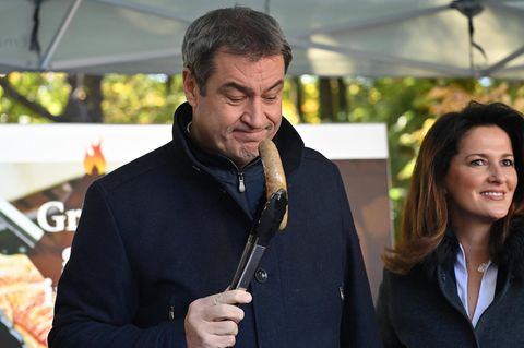 Markus Söder hält eine Wurst mit einer Zange an seine Nase
