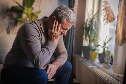 Altersdepressionen: Ein Mann sitzt mit den Armen den Kopf abstützend an einem Fenster